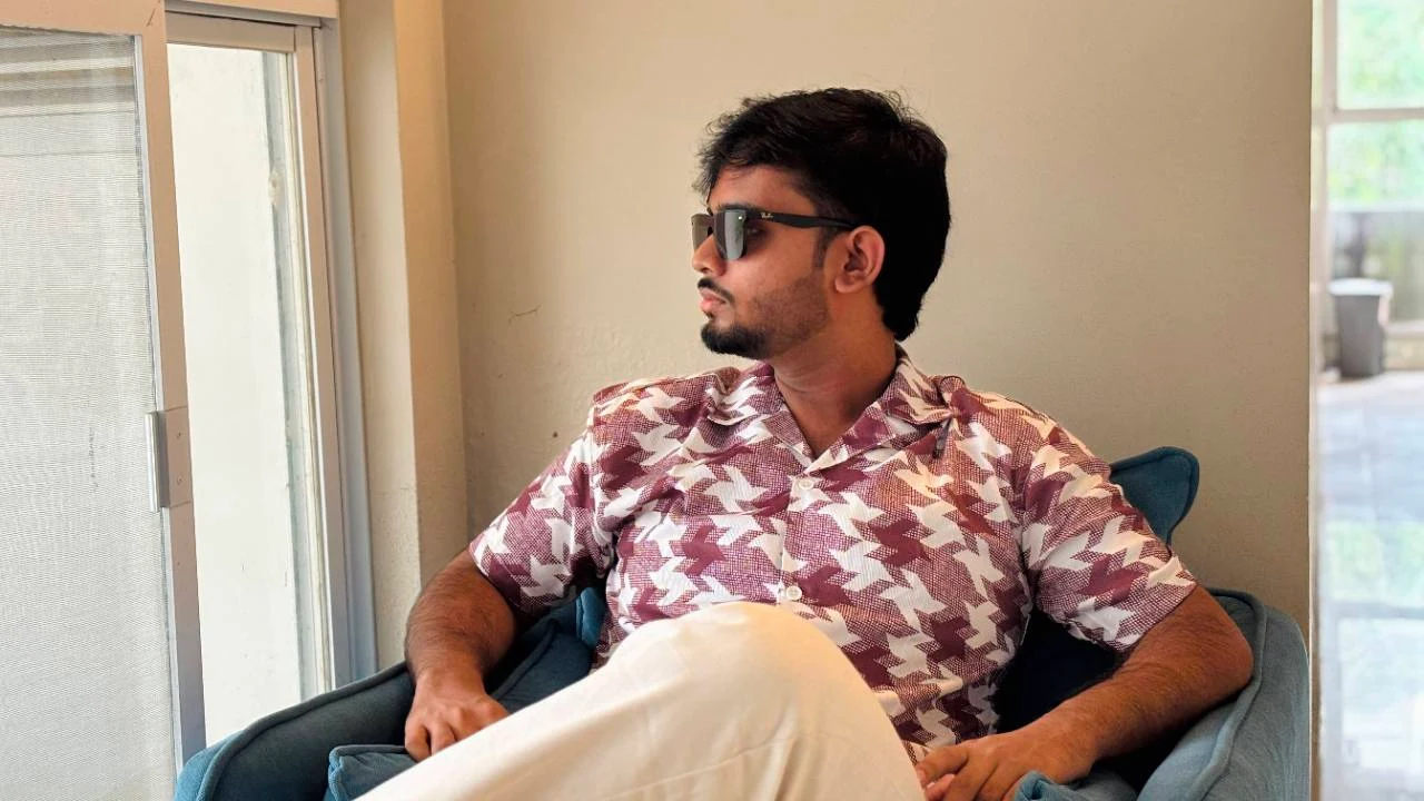 Tanzil Ahmed seated by a window, wearing a patterned shirt and sunglasses.